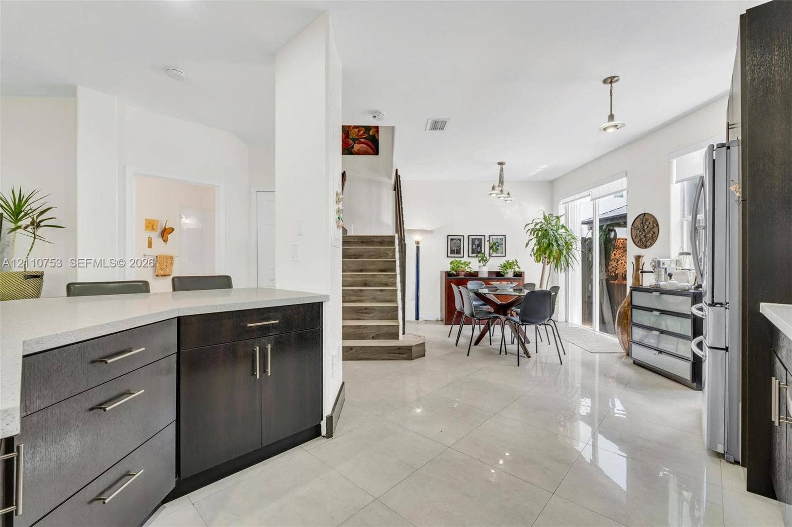 Kitchen featuring dark-finish cabinetry, quartz countertops, and polished tile flooring, with wood-finish stairs and sliding glass doors