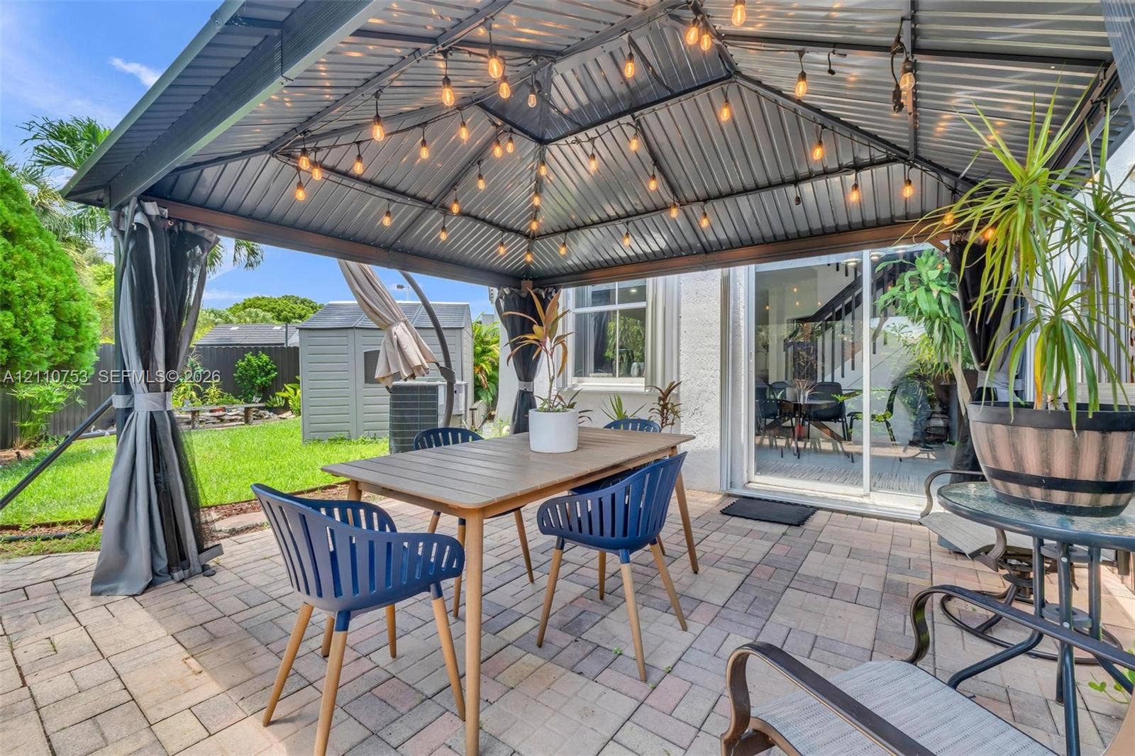 Covered outdoor patio featuring a metal-roof gazebo, paved hardscaping, and string lighting