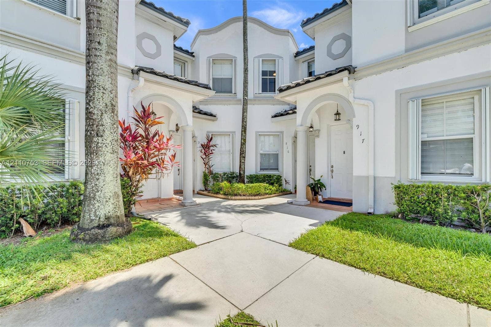 Stucco exterior featuring arched entryways with columns, decorative roofline detailing, and manicured landscaping
