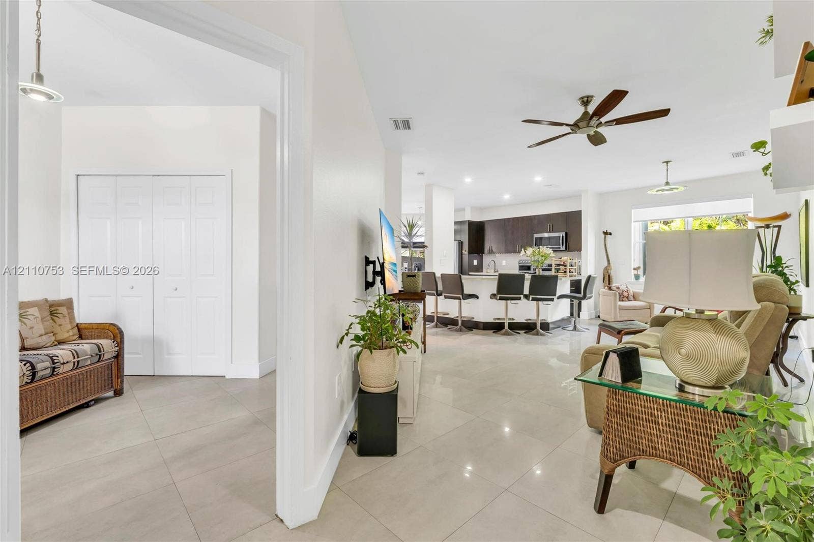 Open-concept interior featuring large-format tile flooring, a chef's kitchen with dark cabinetry, a curved island with integrated seating, recessed lighting, and a ceiling fan