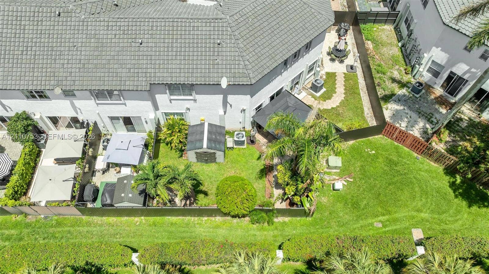 Aerial perspective featuring a private backyard with mature landscaping, a paved patio area, and perimeter fencing