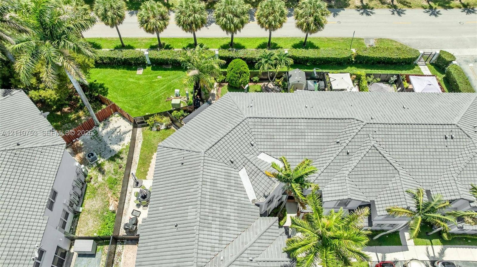 Aerial perspective of a multi-unit property featuring grey tile roofing, expansive manicured lawn space, mature palm trees, and perimeter shrubbery