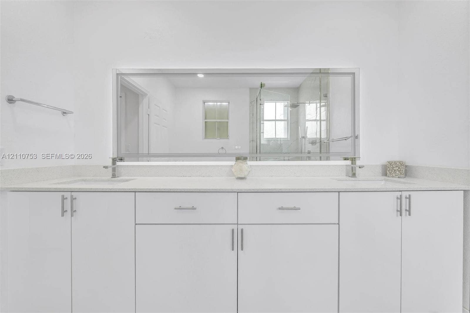 Double vanity with white cabinetry, solid surface countertop, undermount sinks, and a full-width framed mirror