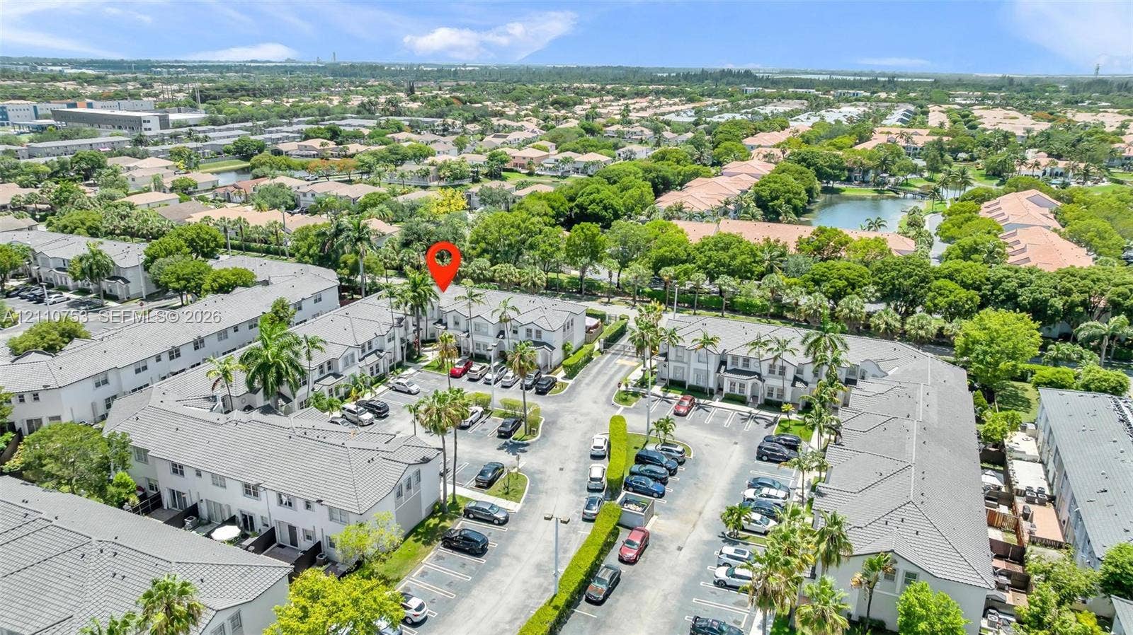 Aerial perspective of multi-family community featuring paved surface parking, mature palm trees, and manicured landscaping