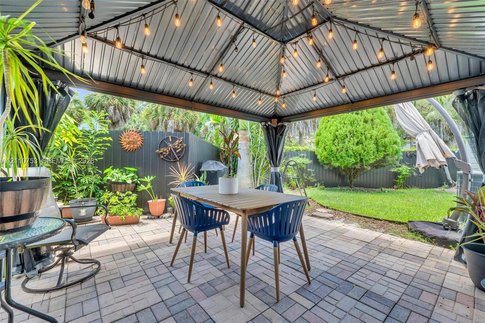 Covered outdoor pavilion featuring a metal roof, string lighting, paver patio, and privacy fencing