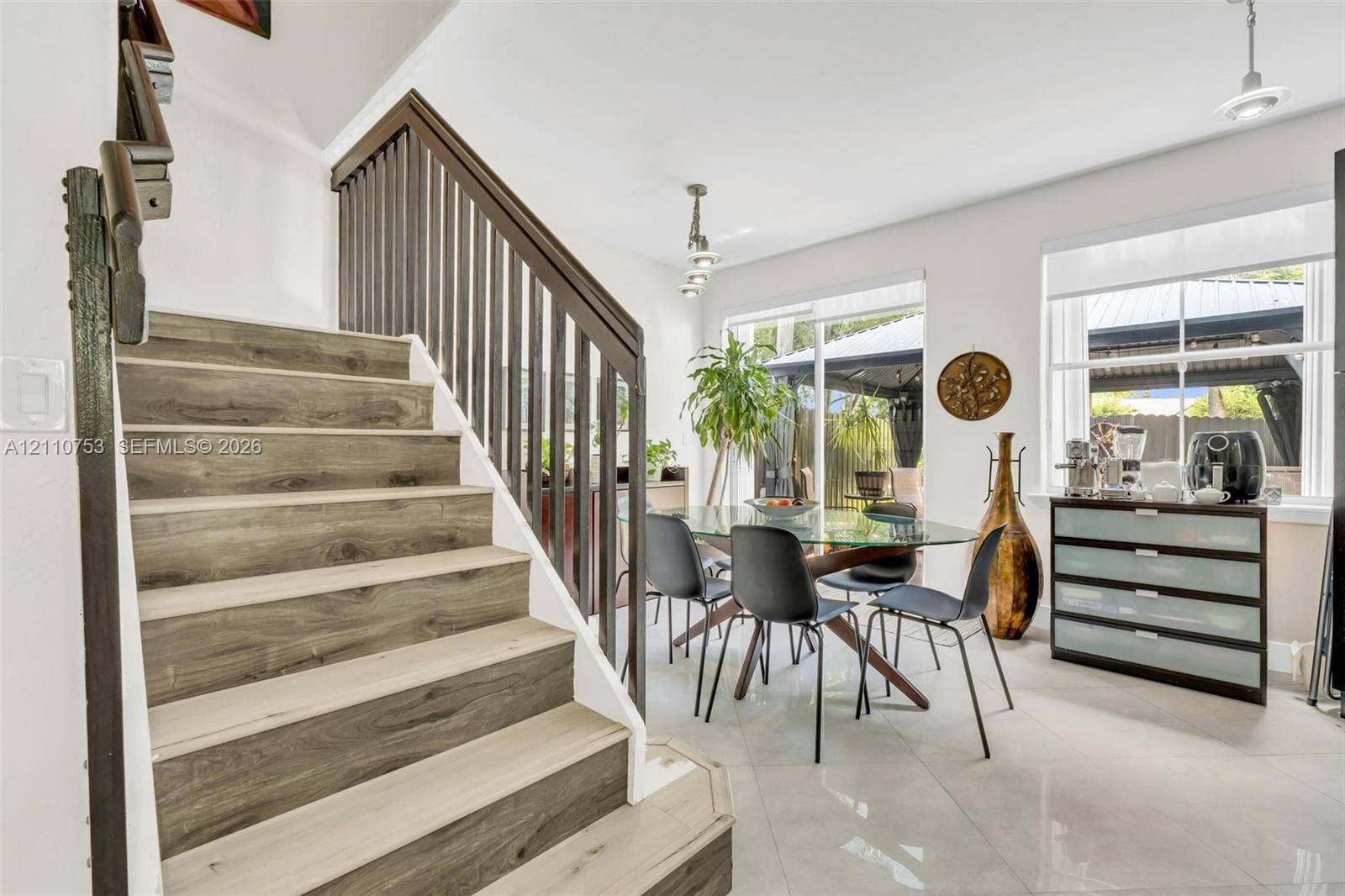 Staircase featuring wood-finish treads and dark vertical metal balusters, large-format tile flooring, multi-pane windows, and modern pendant lighting