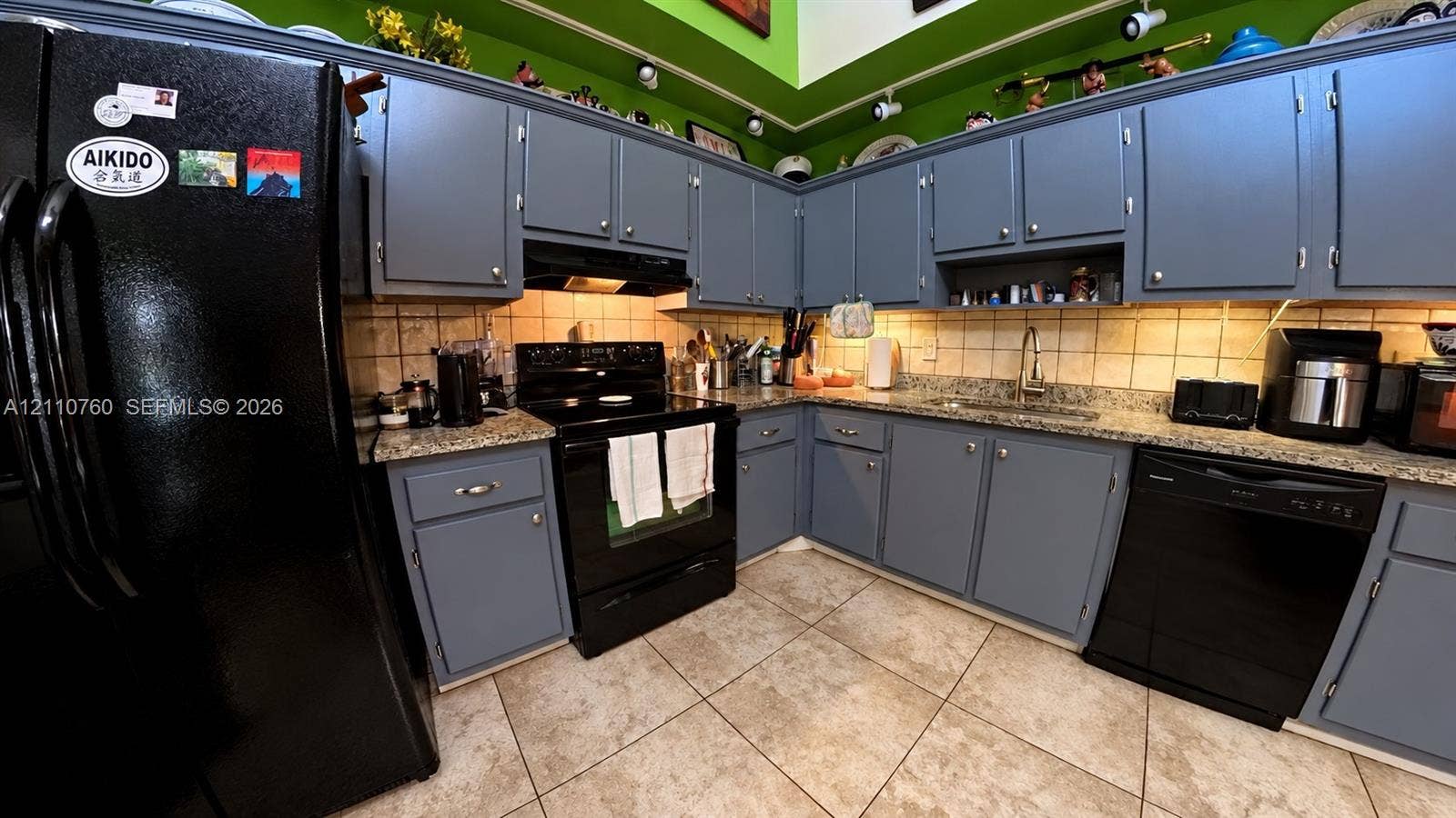 Kitchen featuring solid-color cabinetry, stone-surface countertops, tile backsplash, built-in black appliances, and tile flooring