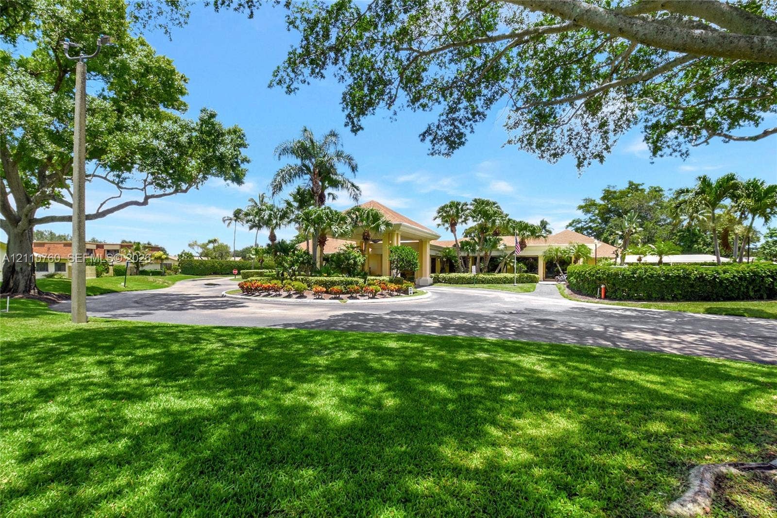 Circular driveway featuring mature tropical landscaping, a covered porte-cochre, and manicured lawns