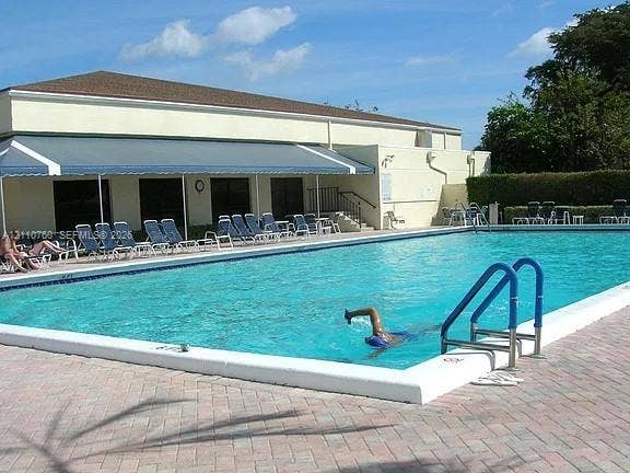 Full-sized swimming pool with white coping, retractable fabric awning, and perimeter paver decking