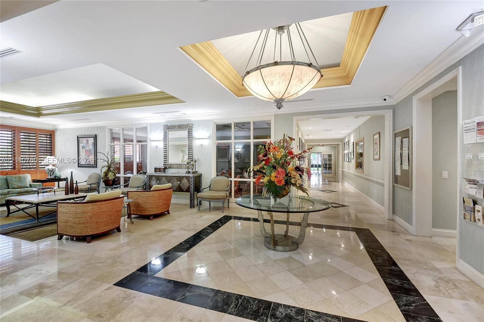 Polished stone flooring with decorative geometric inlay, recessed tray ceiling, and grand pendant lighting fixture