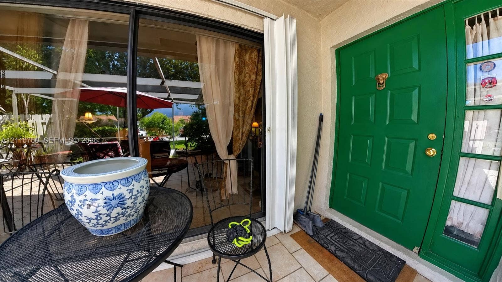 Covered patio featuring ceramic tile flooring, solid-panel green entry door with side light, and expansive sliding glass doors