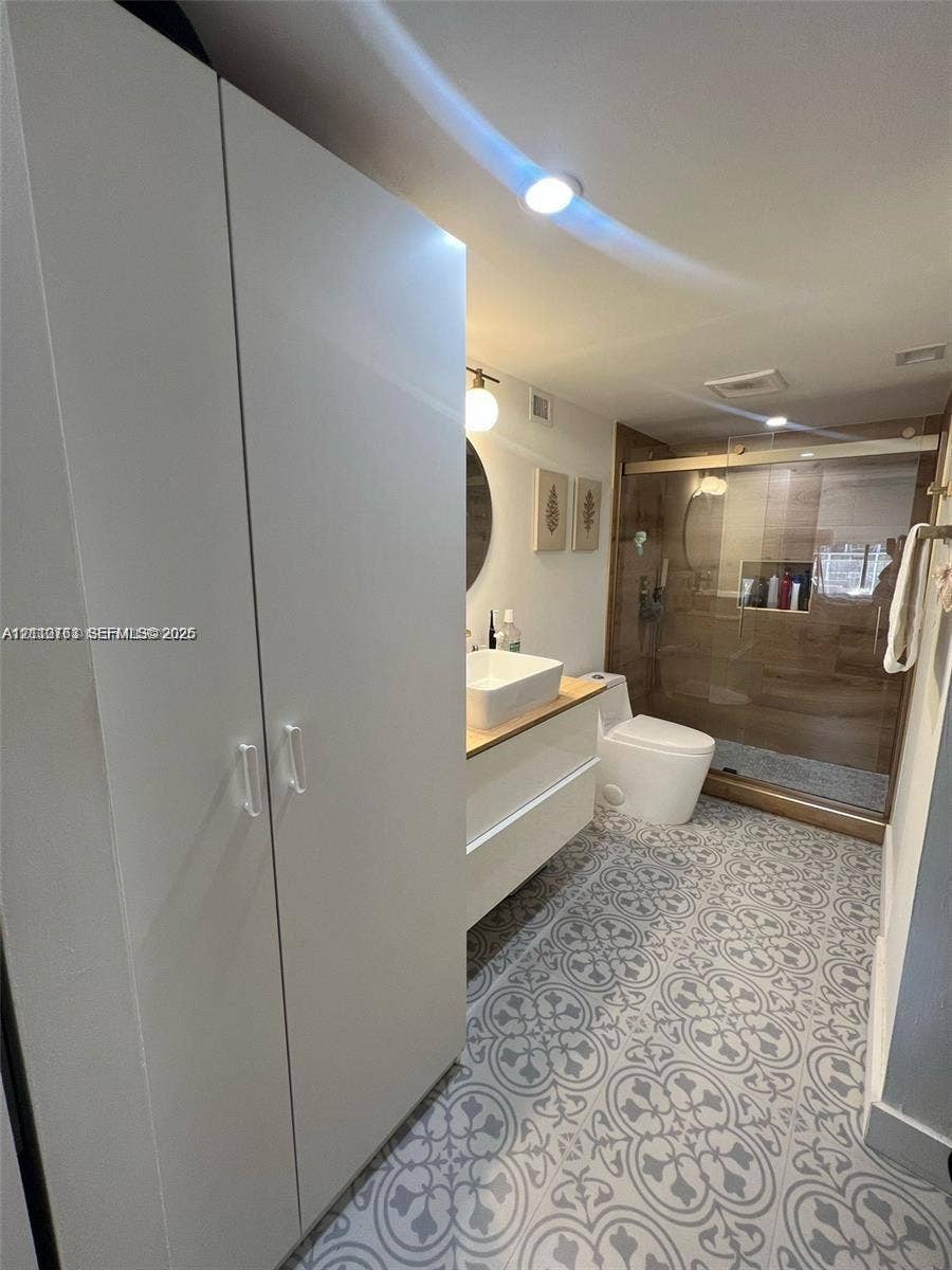 1901 Brickell Avenue, #B1706, Miami, FL 33129 Bathroom featuring a white floating vanity with a vessel sink, patterned tile flooring, built-in floor-to-ceiling cabinetry, and a walk-in shower with glass enclosure