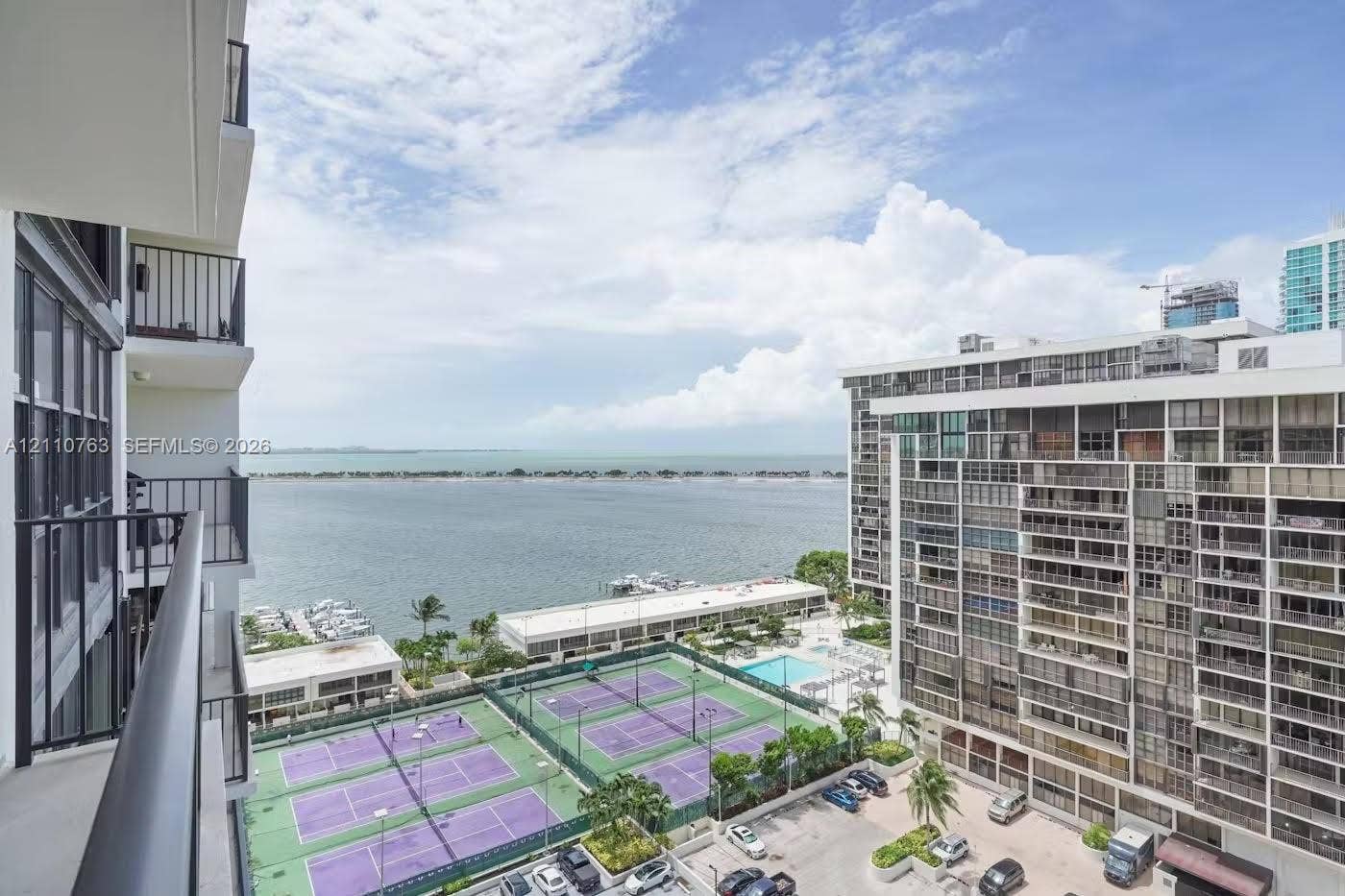 1901 Brickell Avenue, #B1706, Miami, FL 33129 Covered balcony with black metal railings, overlooking tennis courts, a swimming pool, and a coastal waterway