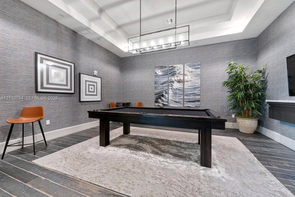 Textured grey wall covering, tray ceiling, rectangular linear pendant light fixture, and dark wood-finish tile flooring