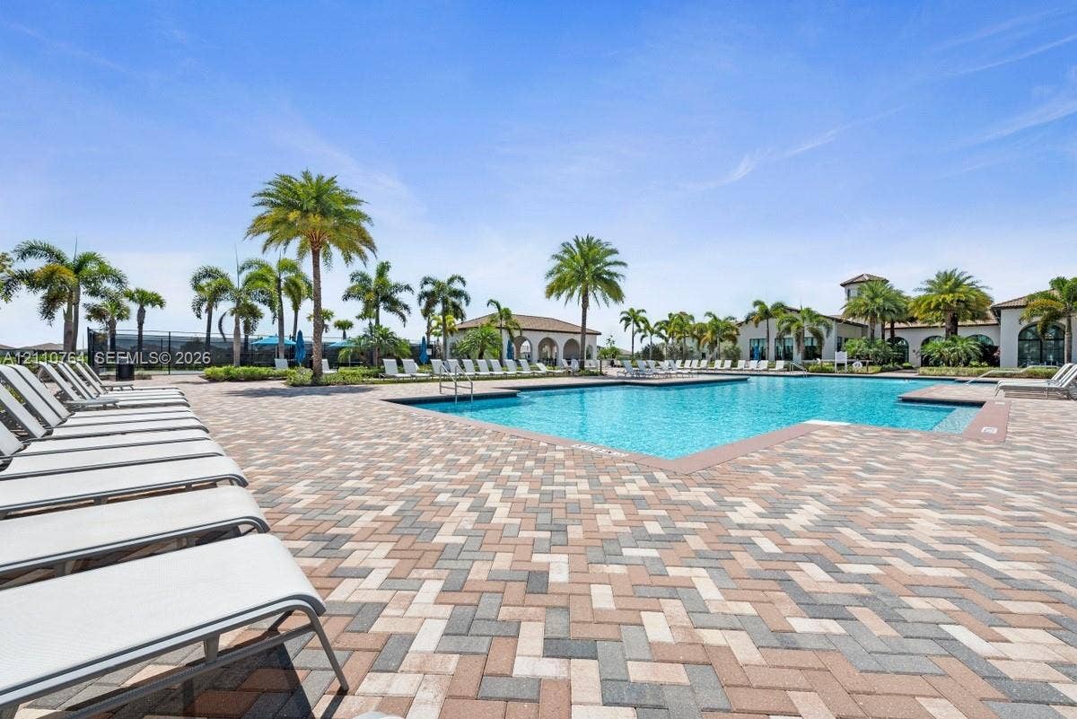 Swimming pool featuring brick paver decking, surrounding palm trees, and an arched pavilion