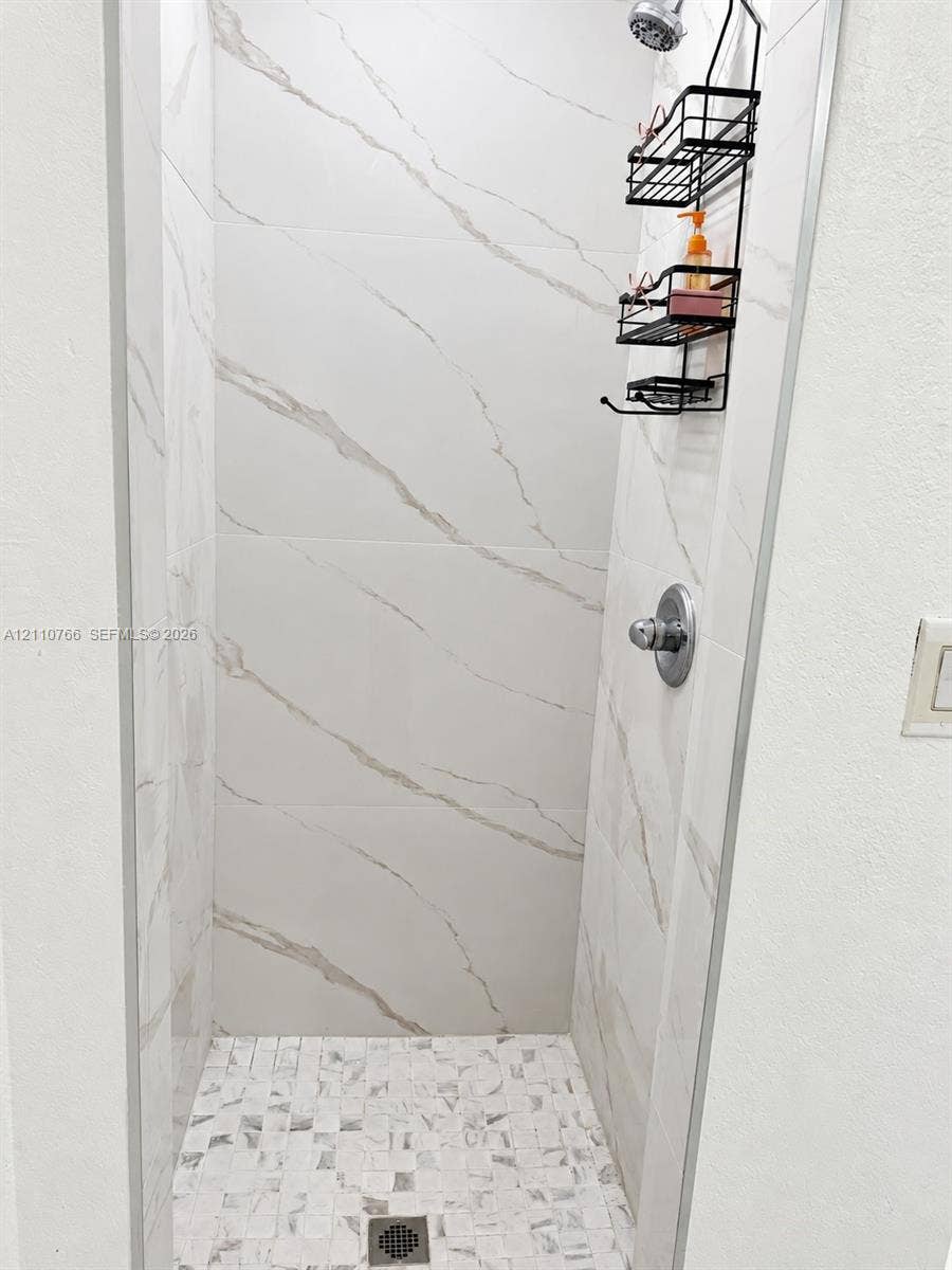 Walk-in shower featuring large-format stone-patterned wall tile, mosaic tile flooring, and a chrome-finish shower valve