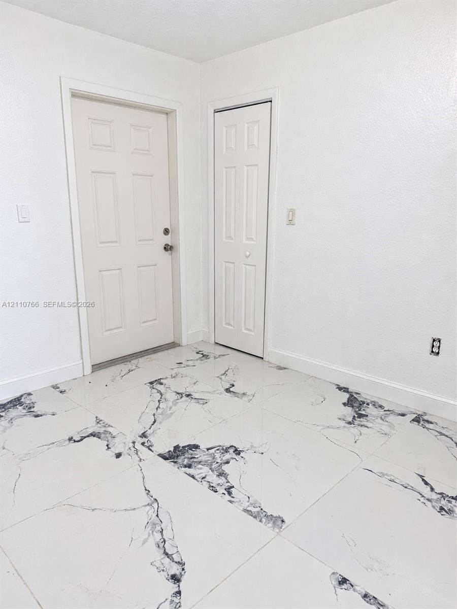 Large-format tile flooring featuring a high-contrast veined pattern, complemented by a six-panel exterior door and matching six-panel closet door