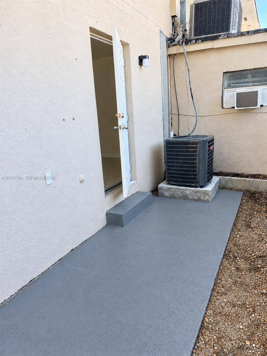 Stucco exterior featuring a dedicated concrete slab, single-step entry, and wall-mounted exterior lighting