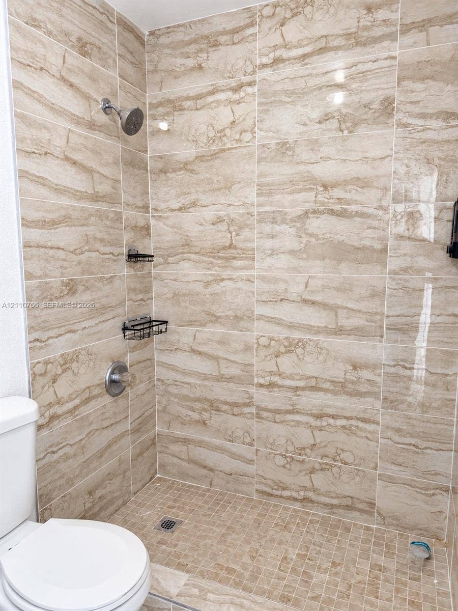Walk-in shower featuring large-format beige tile surround, mosaic tile flooring, built-in metal shelving, and a wall-mounted shower head