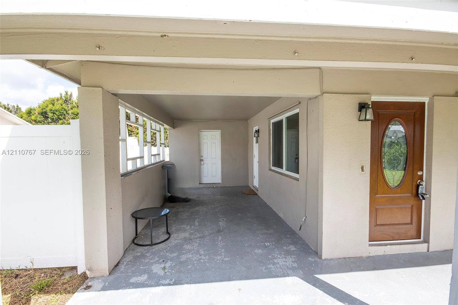 5305 Cleveland Road, Delray Beach, FL 33484 Covered carport with concrete flooring, solid wood-finish entry door featuring a glass oval inlay, and exterior wall-mounted lighting