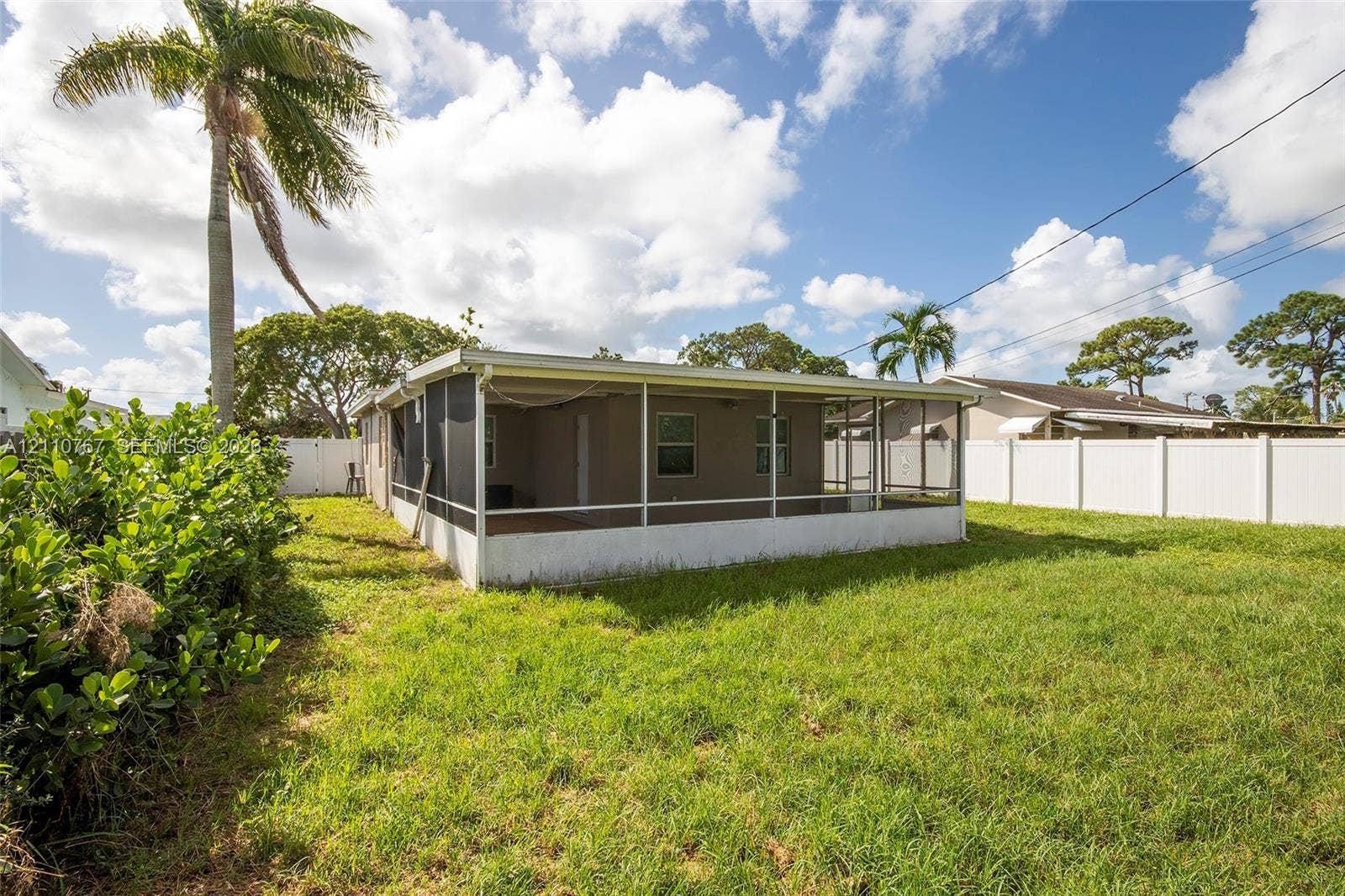 5305 Cleveland Road, Delray Beach, FL 33484 Screened-in rear porch featuring a solid roofline, expansive lawn, and white vinyl perimeter fencing