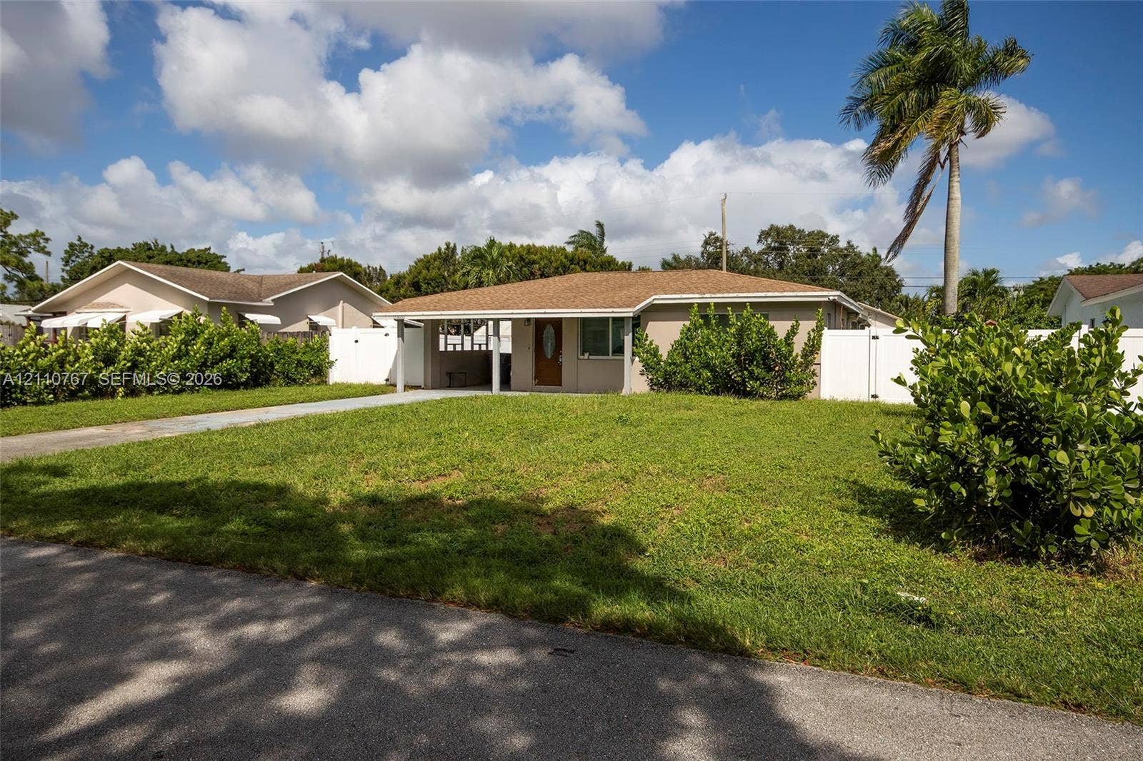 5305 Cleveland Road, Delray Beach, FL 33484 Single-story residence featuring a covered front entryway, shingled roof, stucco exterior, paved driveway, and perimeter white vinyl fencing