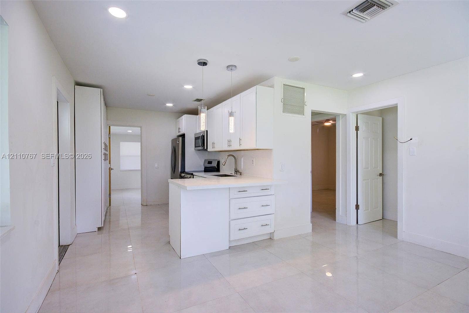 5305 Cleveland Road, Delray Beach, FL 33484 Kitchen featuring white shaker-style cabinetry, solid-surface countertops, dual pendant lighting, stainless steel appliances, and tile flooring