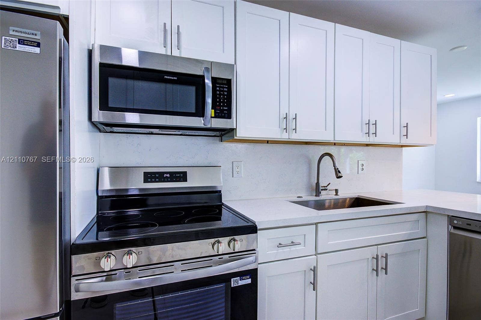 5305 Cleveland Road, Delray Beach, FL 33484 Kitchen featuring white shaker-style cabinetry, stainless steel appliances, white solid-surface countertops, and a single-basin undermount sink with a pull-down faucet