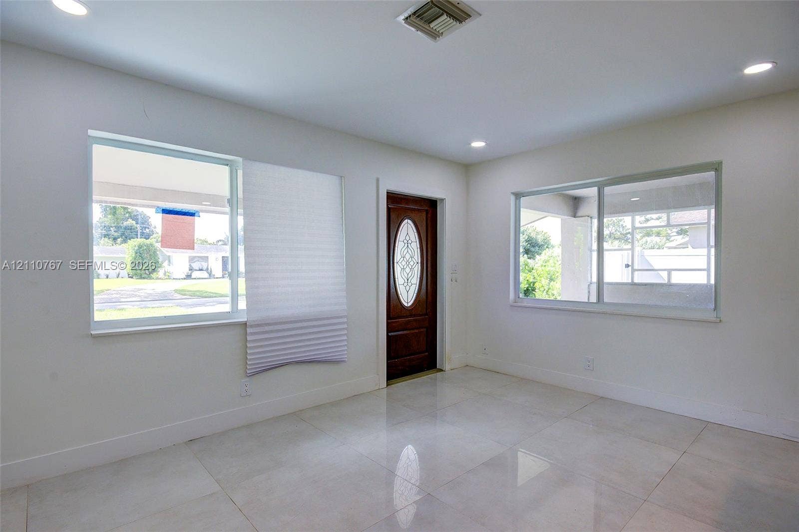 5305 Cleveland Road, Delray Beach, FL 33484 Interior space featuring large-format tile flooring, recessed ceiling lighting, two expansive windows, and a wood-finish entry door with an oval glass insert