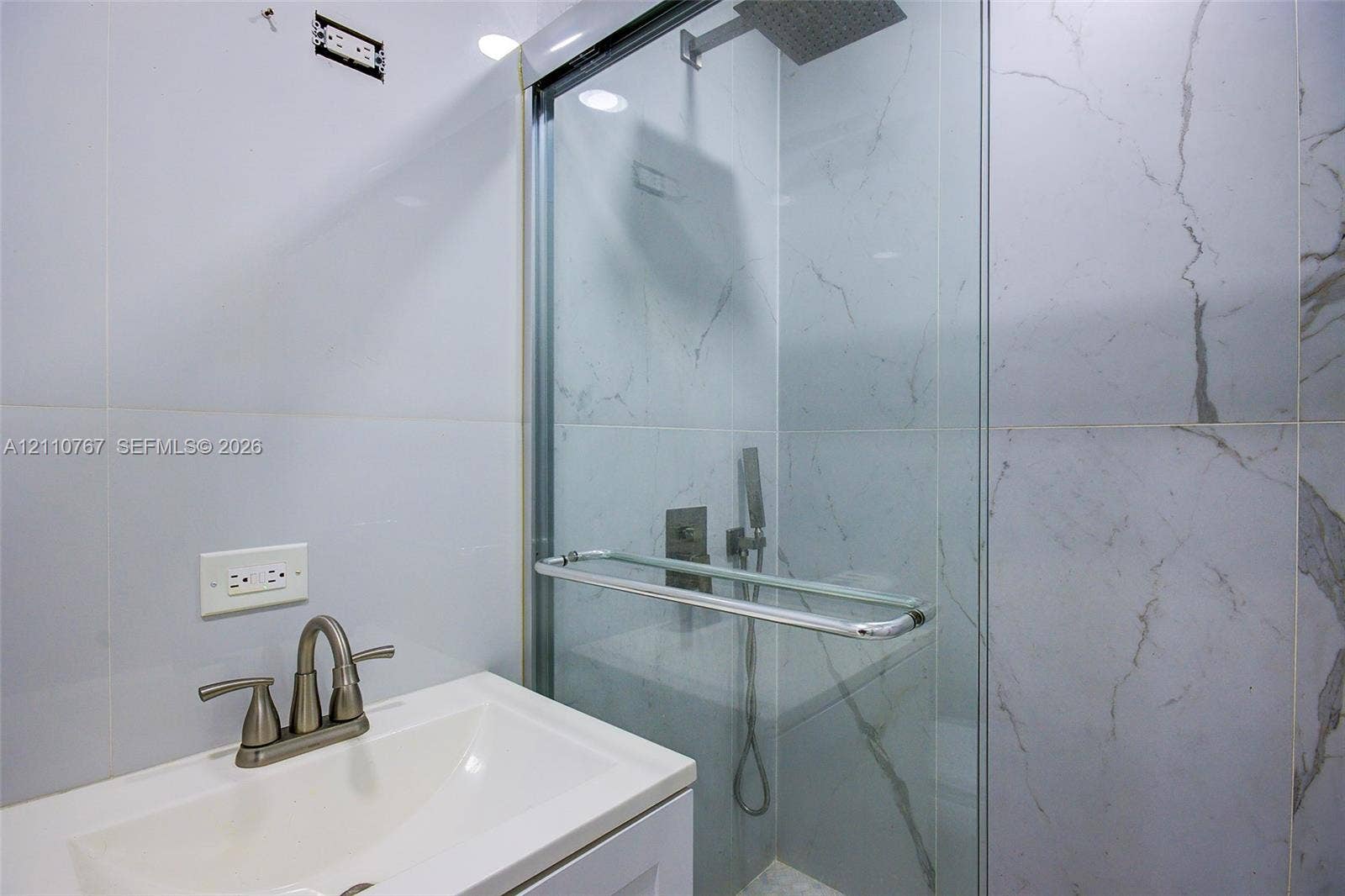 5305 Cleveland Road, Delray Beach, FL 33484 Walk-in shower with a glass enclosure, rainfall showerhead, handheld sprayer, and large-format tile surround, featuring a vanity with a white basin and metallic hardware