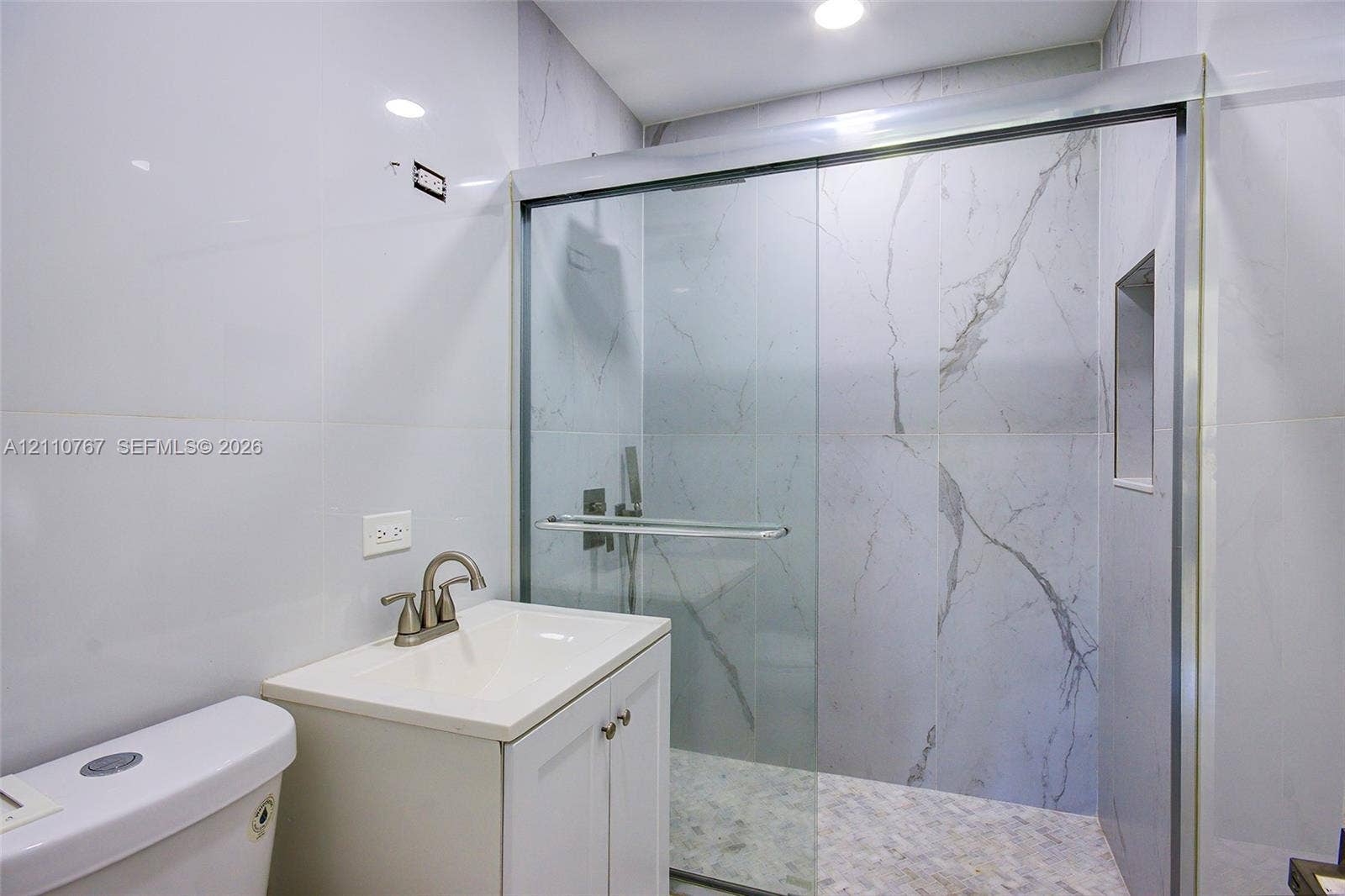 5305 Cleveland Road, Delray Beach, FL 33484 Full-height stone-finish wall tile, frameless glass shower enclosure with sliding door, integrated shower niche, modern vanity cabinet with drop-in sink, and brushed-finish faucet