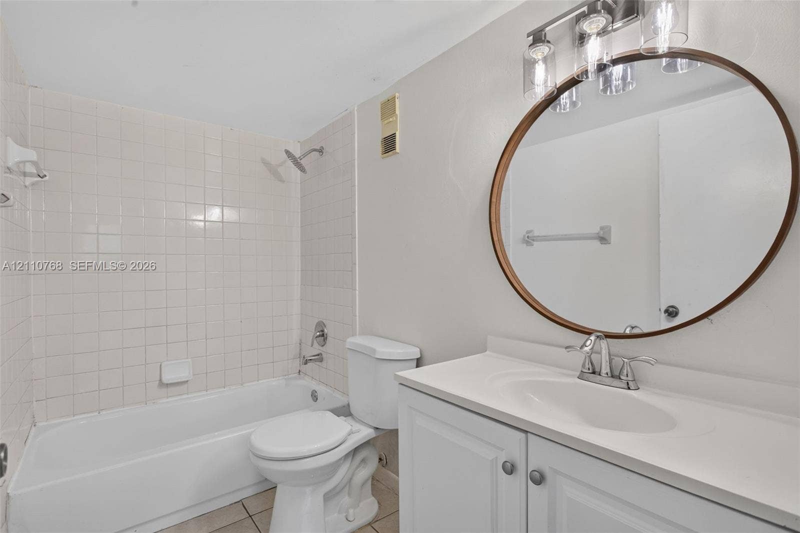 2070 NW 43rd Terrace, #7, Lauderhill, FL 33313 Bathroom featuring a white vanity cabinet with a solid-surface countertop, circular wall-mounted mirror, three-light fixture, and a tiled shower-tub combination