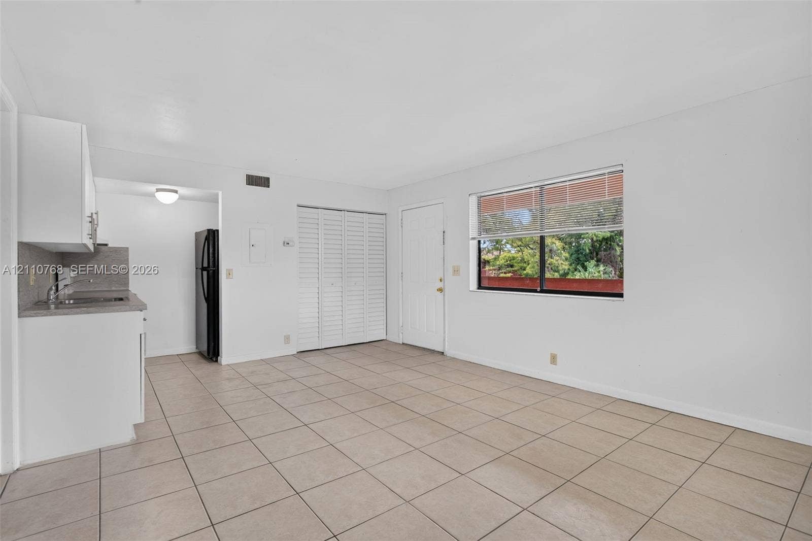 2070 NW 43rd Terrace, #7, Lauderhill, FL 33313 Open living area featuring neutral tile flooring, white cabinetry, louvered closet doors, and large windows with integrated blinds