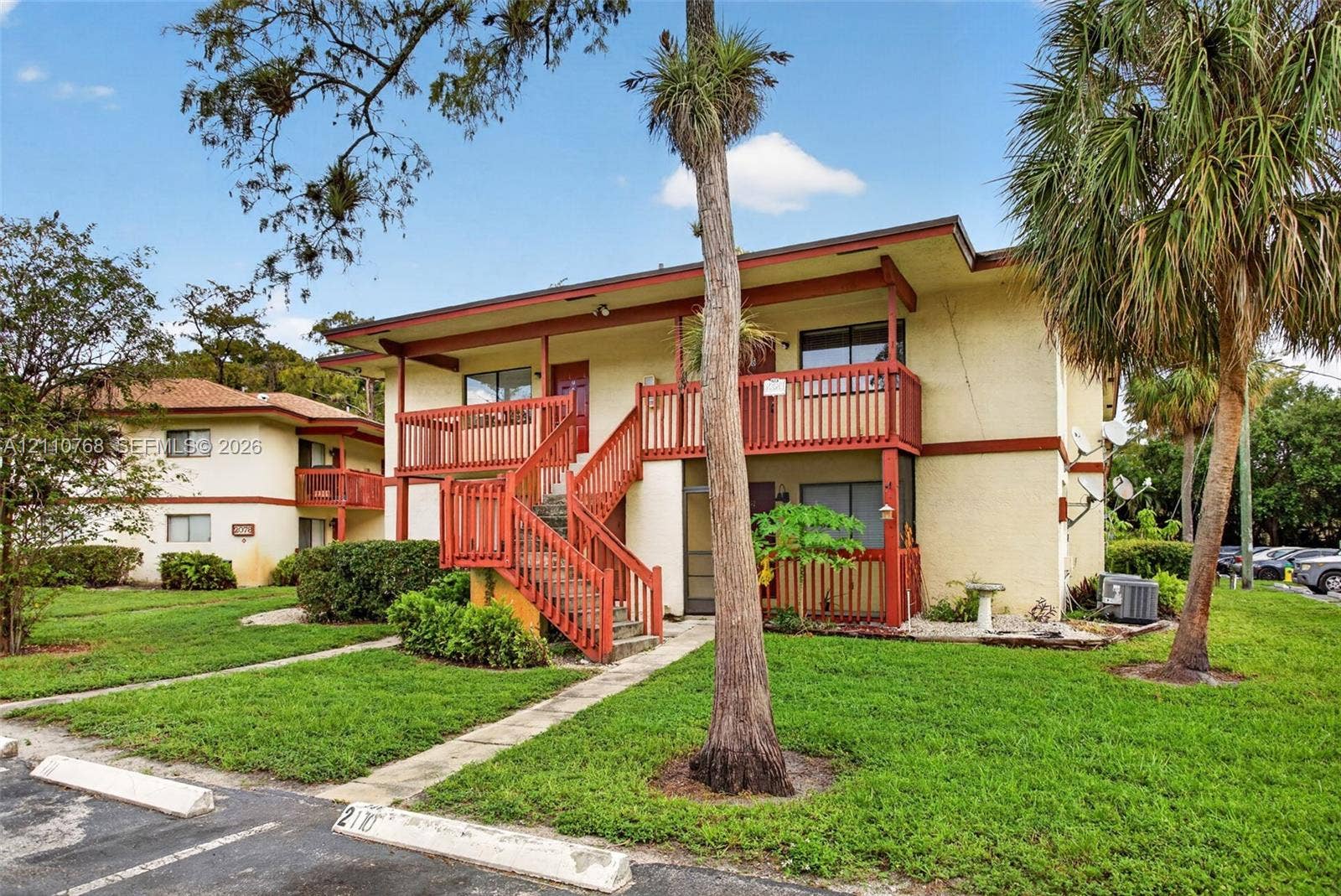 2070 NW 43rd Terrace, #7, Lauderhill, FL 33313 Two-story multi-unit exterior featuring stucco siding, wooden railings, an external staircase, and mature palm trees