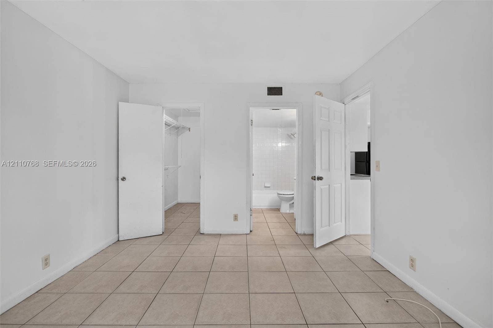 2070 NW 43rd Terrace, #7, Lauderhill, FL 33313 Room interior featuring neutral ceramic tile flooring, two paneled doors, and direct entry points to a walk-in closet and a tiled bathroom