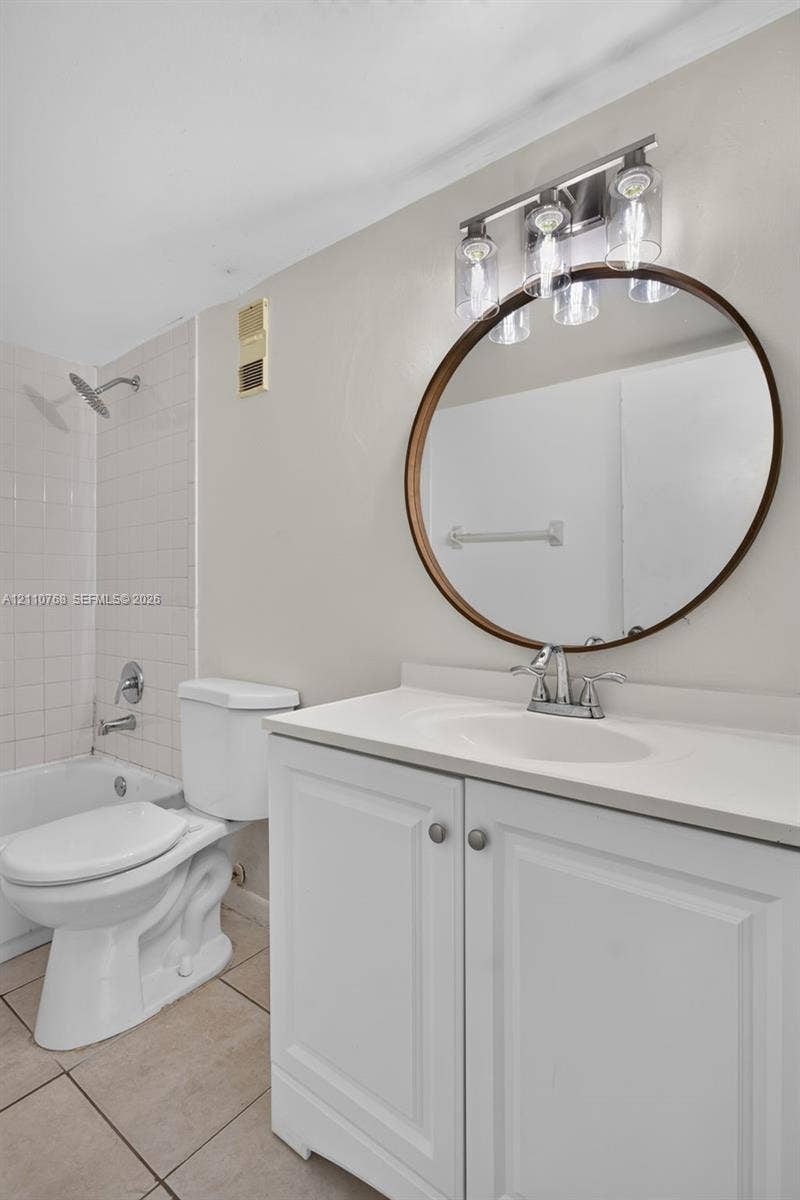 2070 NW 43rd Terrace, #7, Lauderhill, FL 33313 White vanity with a solid-surface countertop and integrated sink, round mirror with a bronze-toned frame, three-light fixture with glass shades, and tiled tub surround