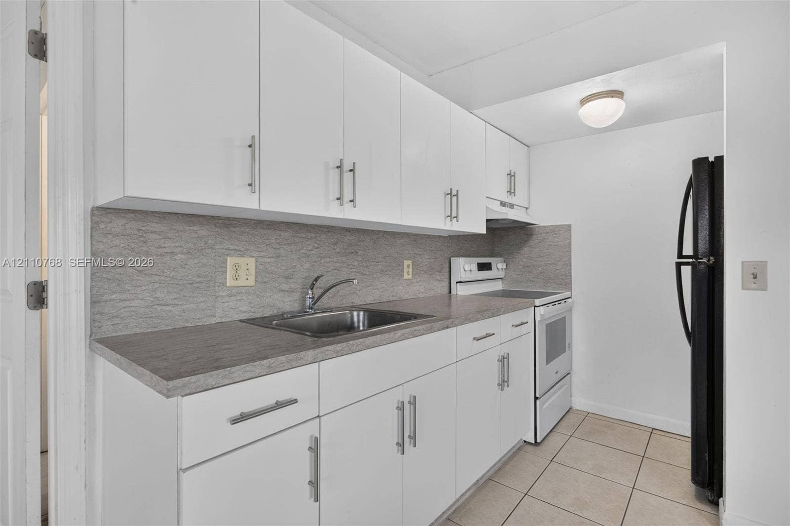 2070 NW 43rd Terrace, #7, Lauderhill, FL 33313 Kitchen featuring white cabinetry with metallic pulls, gray stone-pattern backsplash, neutral countertop, and tile flooring