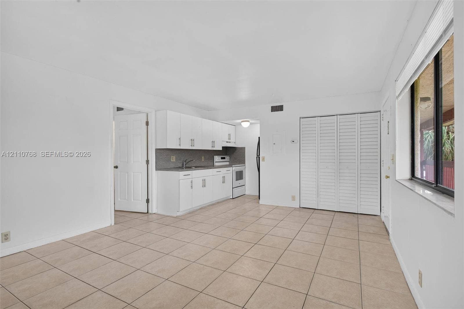 2070 NW 43rd Terrace, #7, Lauderhill, FL 33313 Kitchen featuring white cabinetry, solid-surface countertops, tile backsplash, and tile flooring, including a built-in louvered-door closet