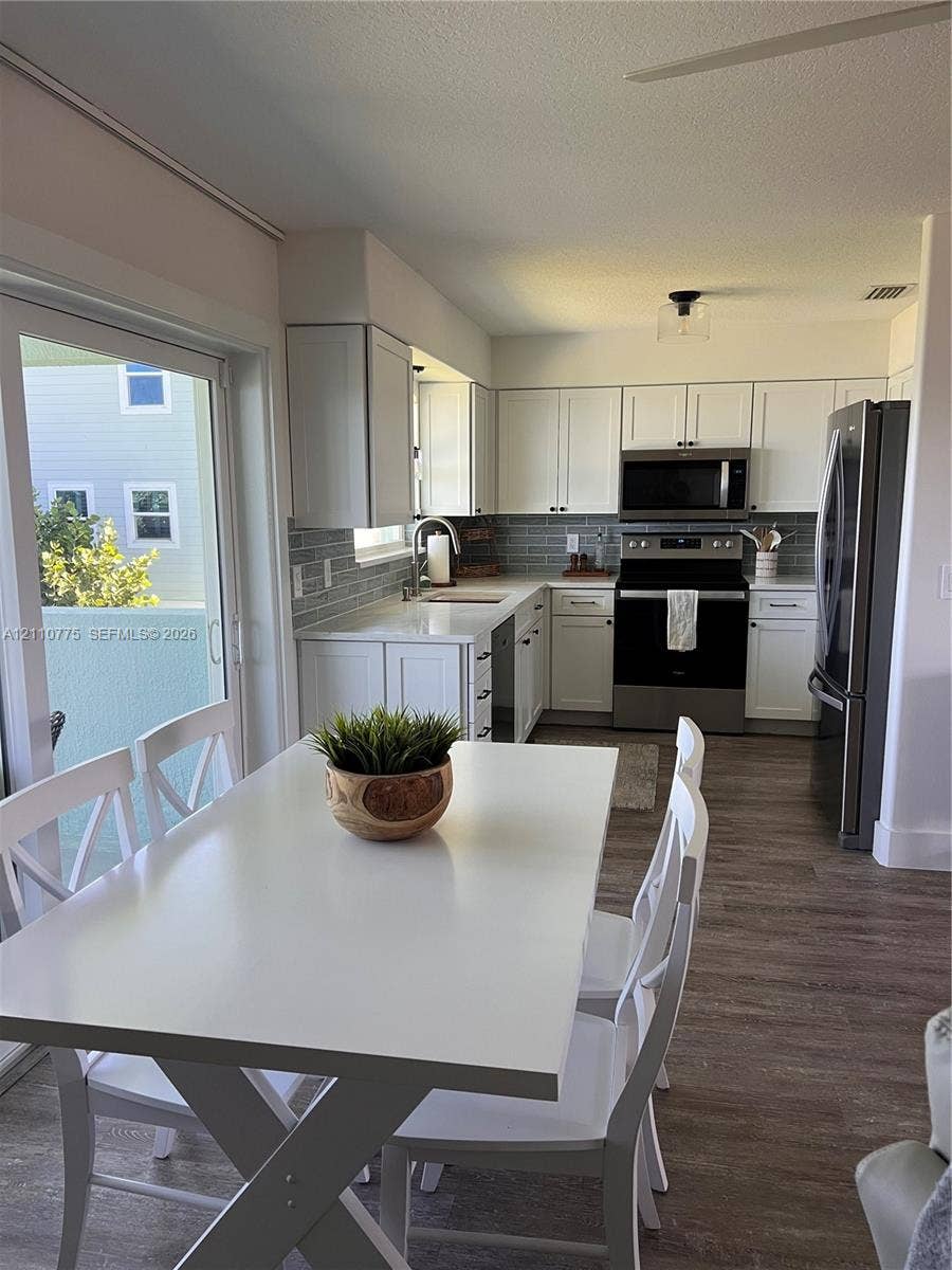 4995 S Highway A1a, #D, Melbourne Beach, FL 32951 Kitchen featuring white cabinetry, solid-surface countertops, subway tile backsplash, stainless steel appliances, and wood-finish flooring