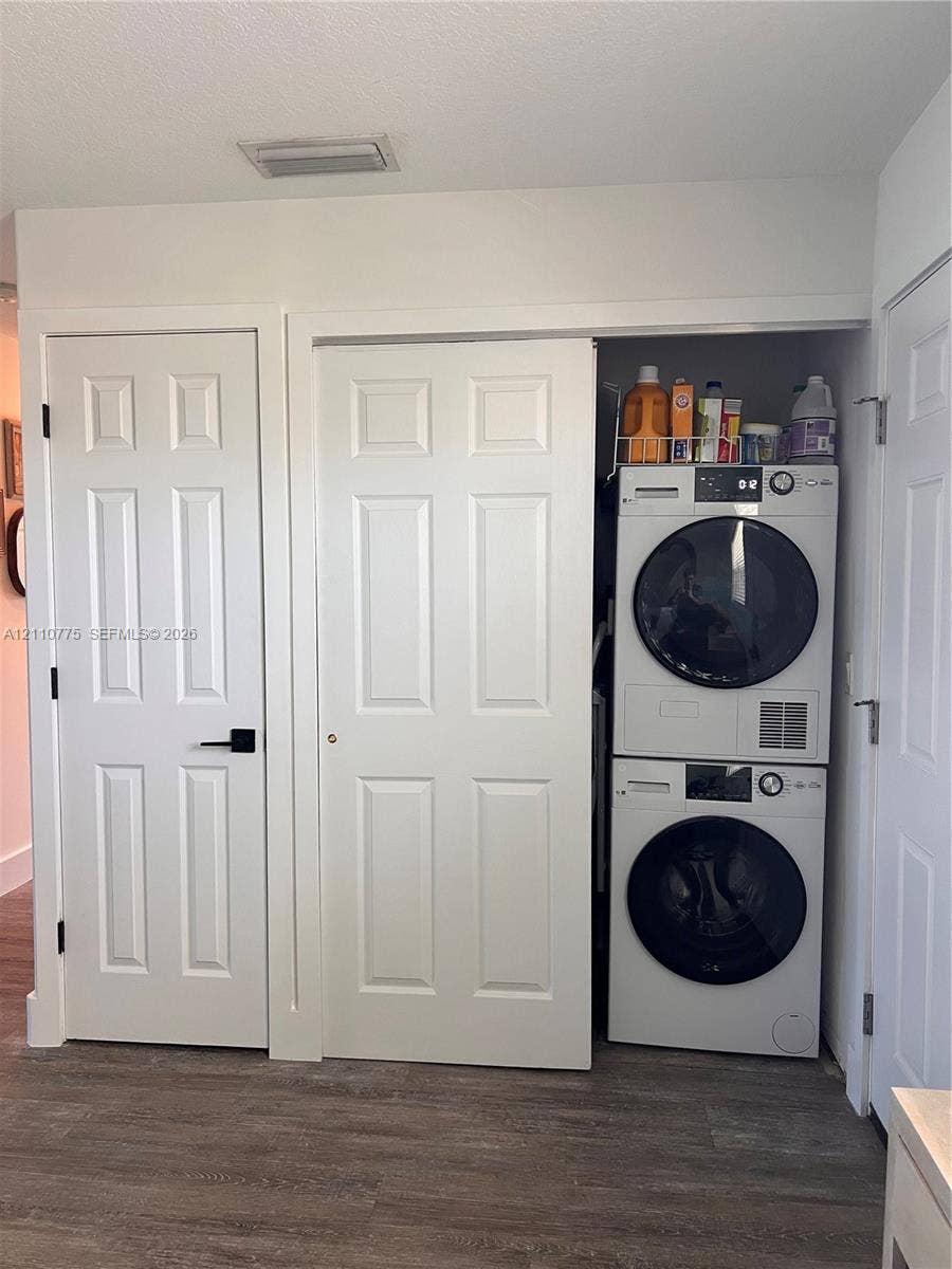 4995 S Highway A1a, #D, Melbourne Beach, FL 32951 Laundry closet featuring stacked high-efficiency appliances, white paneled interior doors, matte black hardware, and wood-finish flooring