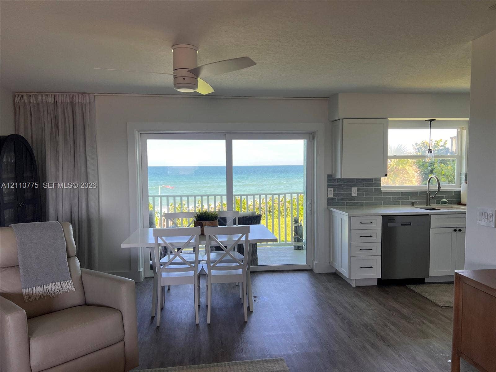 4995 S Highway A1a, #D, Melbourne Beach, FL 32951 Kitchen featuring white shaker-style cabinetry, grey subway tile backsplash, stainless steel dishwasher, and wood-finish flooring, with sliding glass doors opening to an exterior balcony