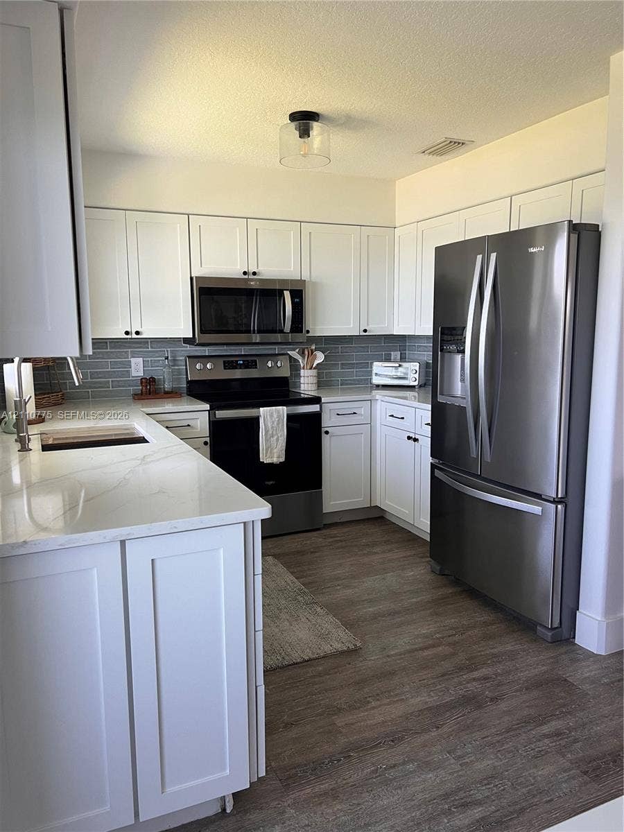 4995 S Highway A1a, #D, Melbourne Beach, FL 32951 Kitchen featuring white shaker-style cabinetry, quartz countertops, subway tile backsplash, stainless steel appliances, and wood-finish flooring