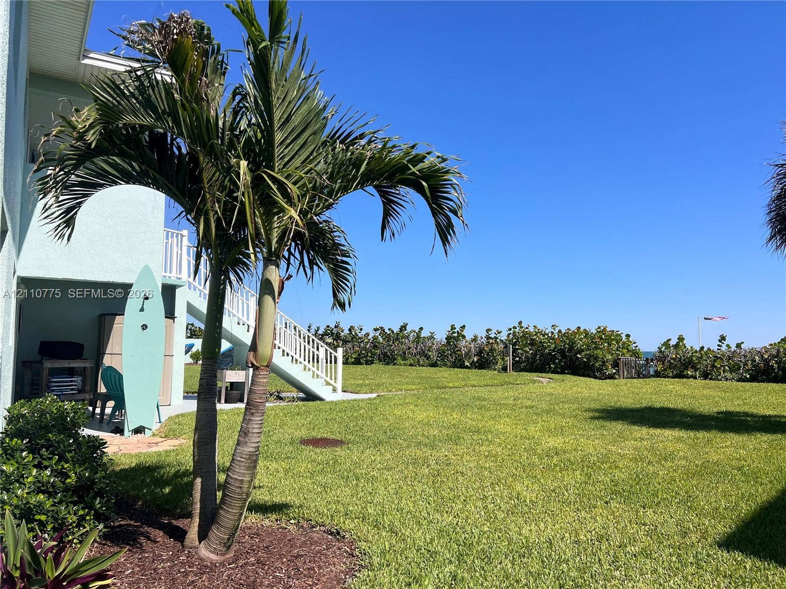 4995 S Highway A1a, #D, Melbourne Beach, FL 32951 Expansive lawn featuring mature palm trees, exterior stairs with white railings, and manicured landscaping