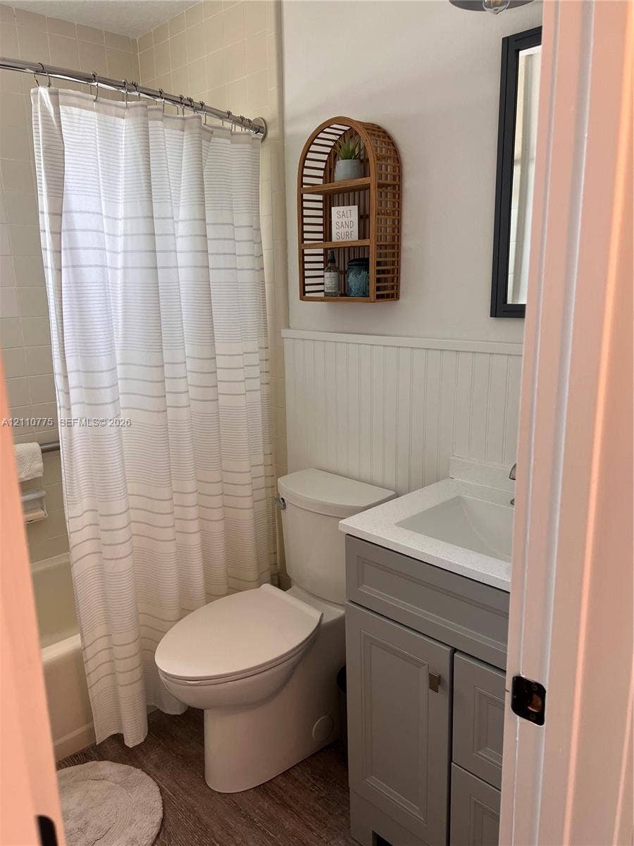 4995 S Highway A1a, #D, Melbourne Beach, FL 32951 Bathroom featuring a grey vanity with a rectangular sink, beadboard wainscoting, a bathtub with tile surround, and wood-finish flooring