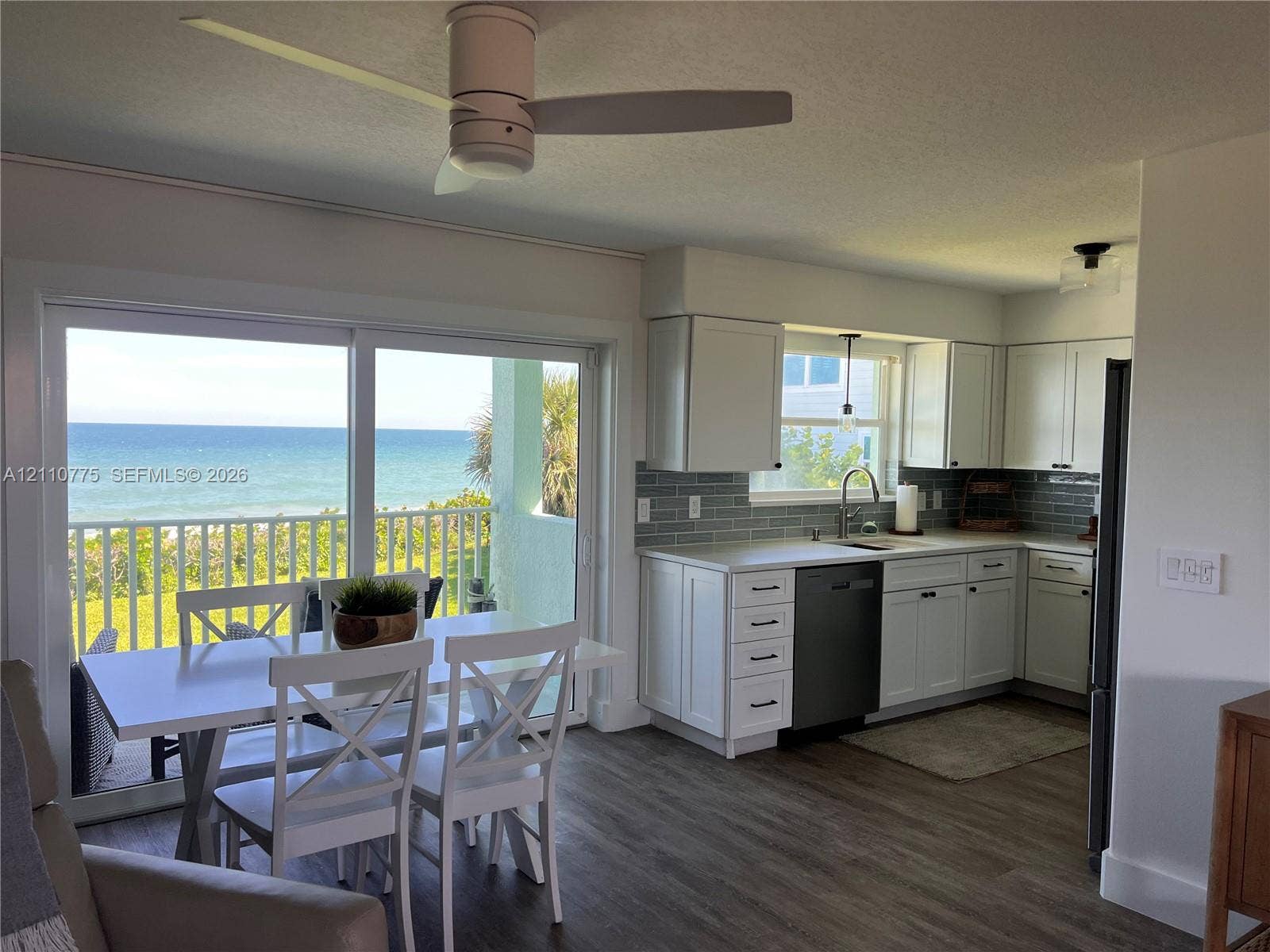 4995 S Highway A1a, #D, Melbourne Beach, FL 32951 Kitchen featuring white shaker cabinetry, grey subway tile backsplash, solid-surface countertops, and wood-finish flooring, with sliding glass doors opening to an ocean backdrop