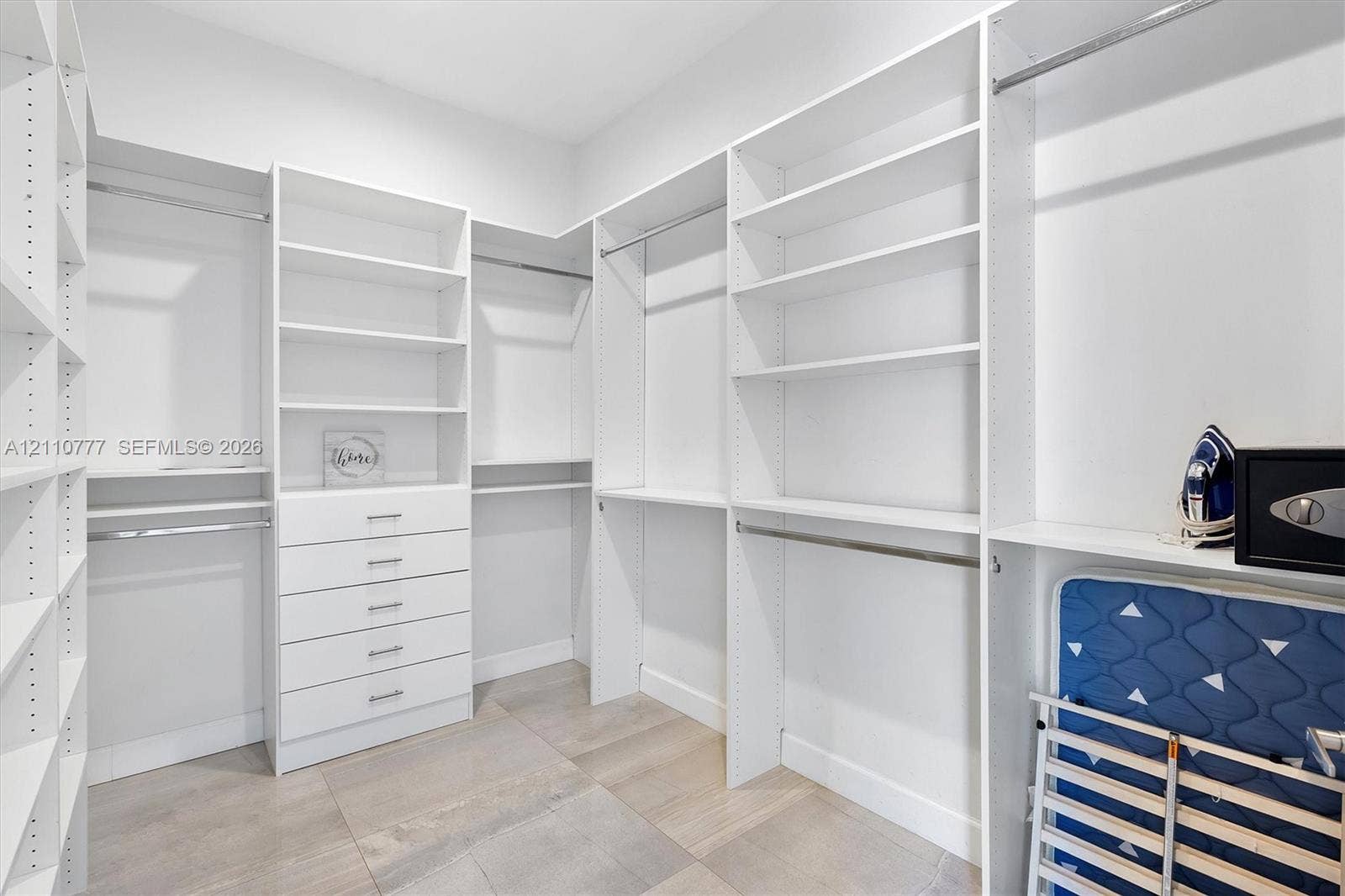 Walk-in closet featuring white built-in shelving, integrated storage drawers with silver-tone pulls, and horizontal garment rods