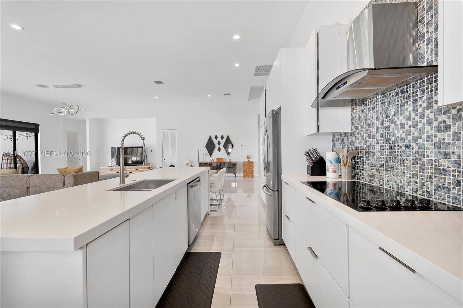 Kitchen featuring flat-panel white cabinetry, quartz countertops, a mosaic tile backsplash, a stainless steel range hood, and large-format tile flooring