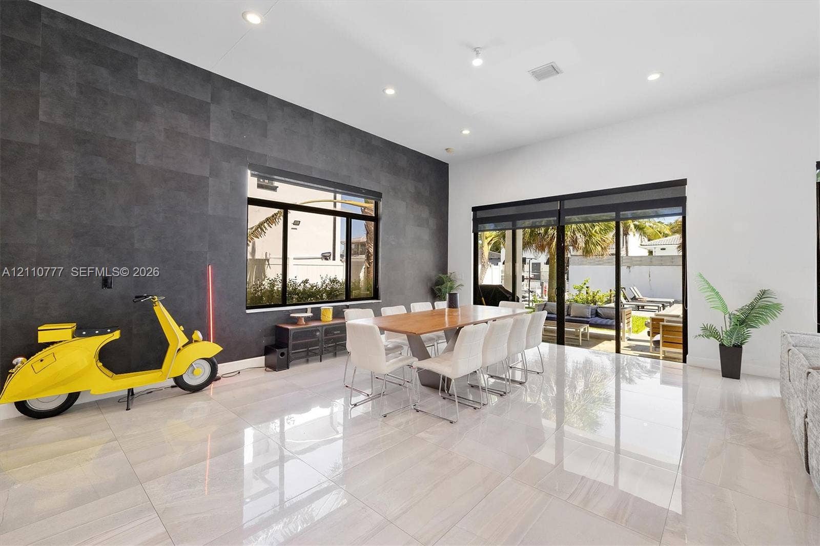 Living area featuring high ceilings, large-format tile flooring, a charcoal-toned accent wall, and sliding glass doors leading to the exterior