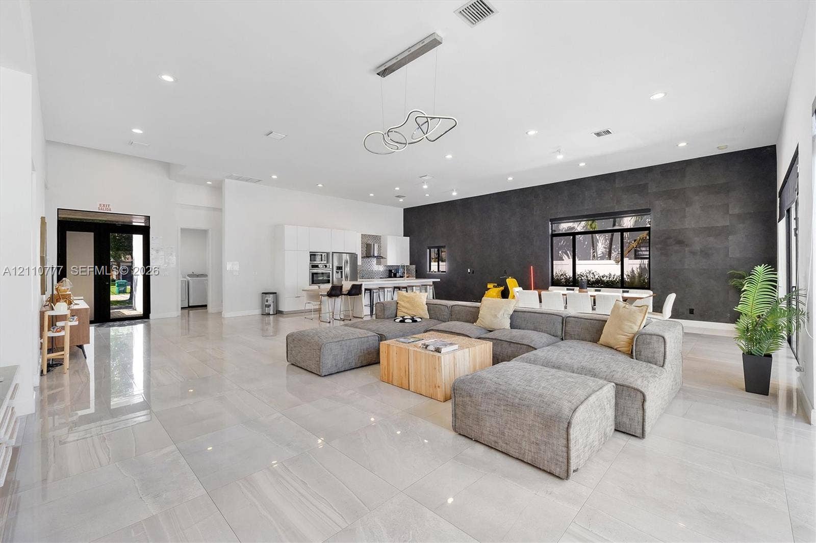 Open-concept living space featuring high ceilings with recessed lighting, large-format tile flooring, a charcoal stone-finish accent wall, and contemporary geometric pendant lighting