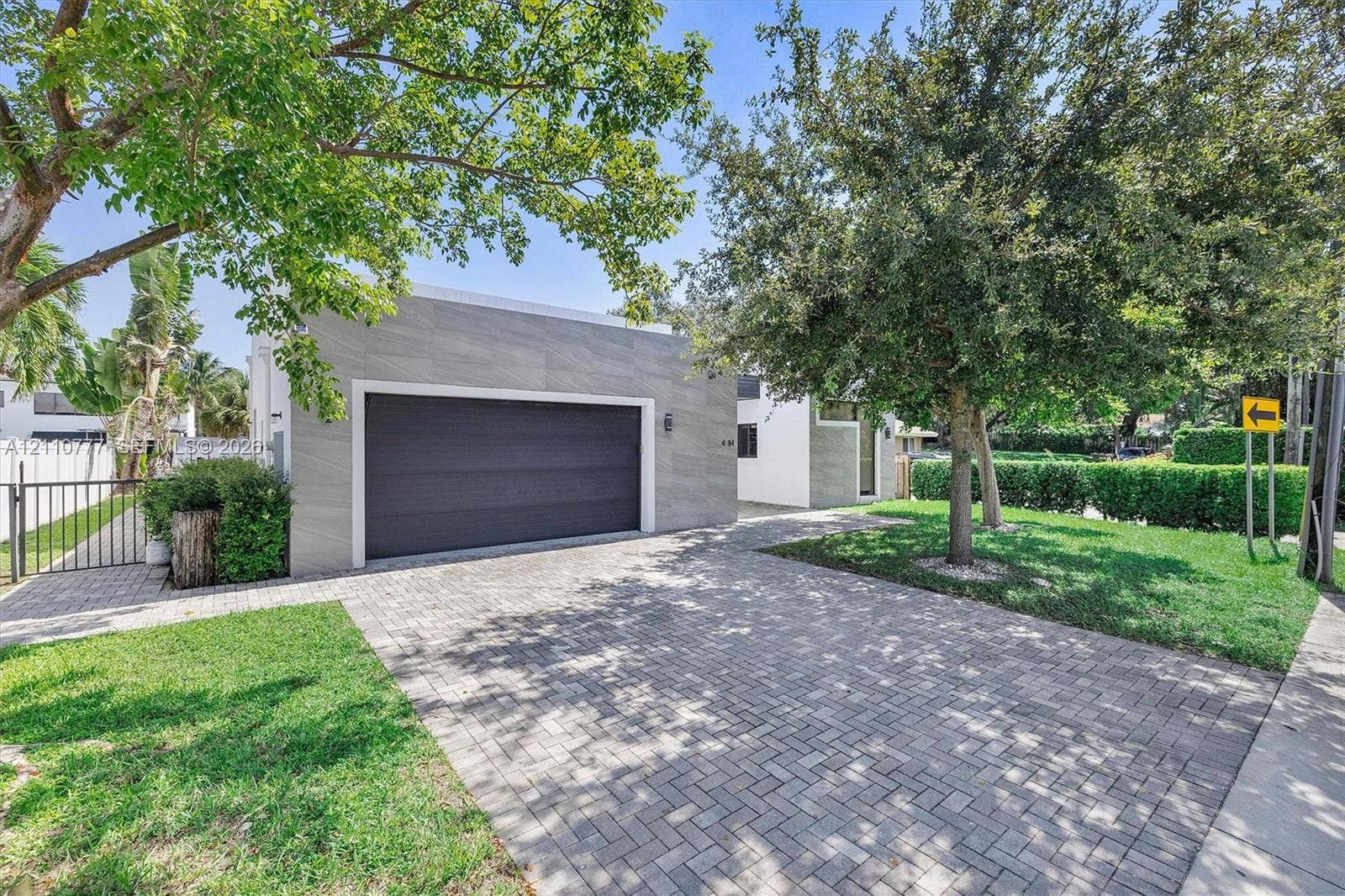 Detached garage with large-format stone-textured exterior cladding, paved brick driveway, metal gate, and manicured landscaping
